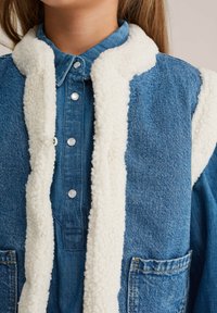 Giacca di denim con colletto in shearling, di colore blu, caratterizzata da bottoni a pressione in perla e tasche sul petto, che mostra una finitura in tessuto testurizzato.