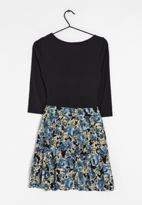 Svart topp med trekvartslånga ärmar, som övergår till en blommig kjol med blå och gröna blommor på en svart bakgrund.