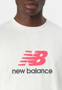 Gray cotton t-shirt featuring a prominent pink and red "N" logo with stylized lines above the text "new balance" in black.