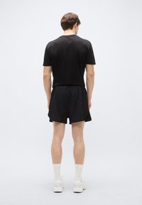 Μαύρο αθλητικό κοντομάνικο τοπ και σορτς, κατασκευασμένα από ελαφρύ ύφασμα. Το σύνολο ολοκληρώνουν λευκά αθλητικά παπούτσια και λευκές κάλτσες μέχρι το γόνατο.