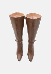 Καφέ δερμάτινα ψηλά μποτάκια μέχρι το γόνατο, με μυτερή μύτη, λεία υφή, κλείσιμο με φερμουάρ και μια διακοσμητική λωρίδα κοντά στον αστράγαλο.