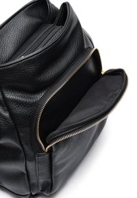 Sac à dos en cuir noir avec des zippers dorées, comportant plusieurs compartiments et une finition texturée. Doublure en tissu lisse dans les poches intérieures.