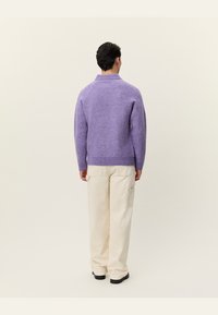 Pulover violet din lână cu gât înalt și tiv cu nervuri, asortat cu pantaloni largi de culoare crem, cu buzunare laterale.