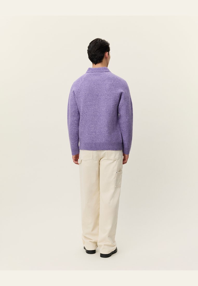 Pulover violet din lână cu gât înalt și tiv cu nervuri, asortat cu pantaloni largi de culoare crem, cu buzunare laterale.