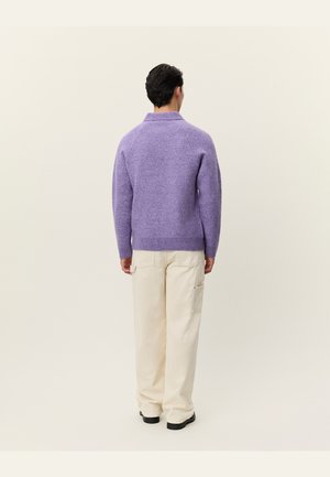 Violetinis vilnonis megztinis su aukštu kaklu ir juostotu apdaila, derinamas su grietinėlės spalvos plačiomis kelnėmis su šoninėmis kišenėmis.