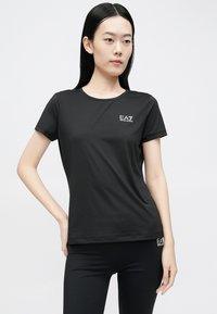 Fekete rövid ujjú póló sima, rugalmas anyagból, kis fehér EA7 logóval a bal mellrészen és kerek nyakkivágással.