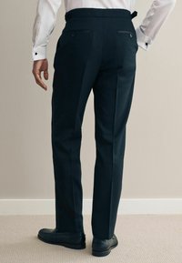 Pantalons noirs ajustés à coupe droite, dotés de deux poches arrière et de passants de ceinture, associés à des chaussures en cuir noires. La texture semble lisse.