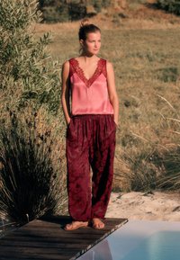 Ermeløs satin top i blush med blondekant, parret med løse, bordeauxmønstrede bukser. Sandaler og naturlig udendørs baggrund.