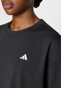 Μαύρο βαμβακερό T-shirt με στρογγυλεμένο γιακά, που διαθέτει λευκό τριγωνικό λογότυπο στην αριστερή πλευρά. Ομαλή υφή, casual σχεδιασμός.