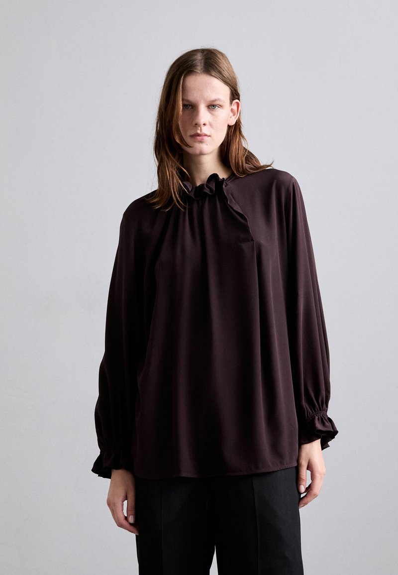 Blusa marrone scuro con collo alto e dettagli a volant, maniche lunghe con polsini arricciati, realizzata in un tessuto leggero e liscio.