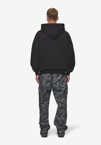 Sweat à capuche noir oversize avec une poche kangourou et une capuche à cordon, associé à un jean ample gris à motif éclaboussures et des baskets foncées.