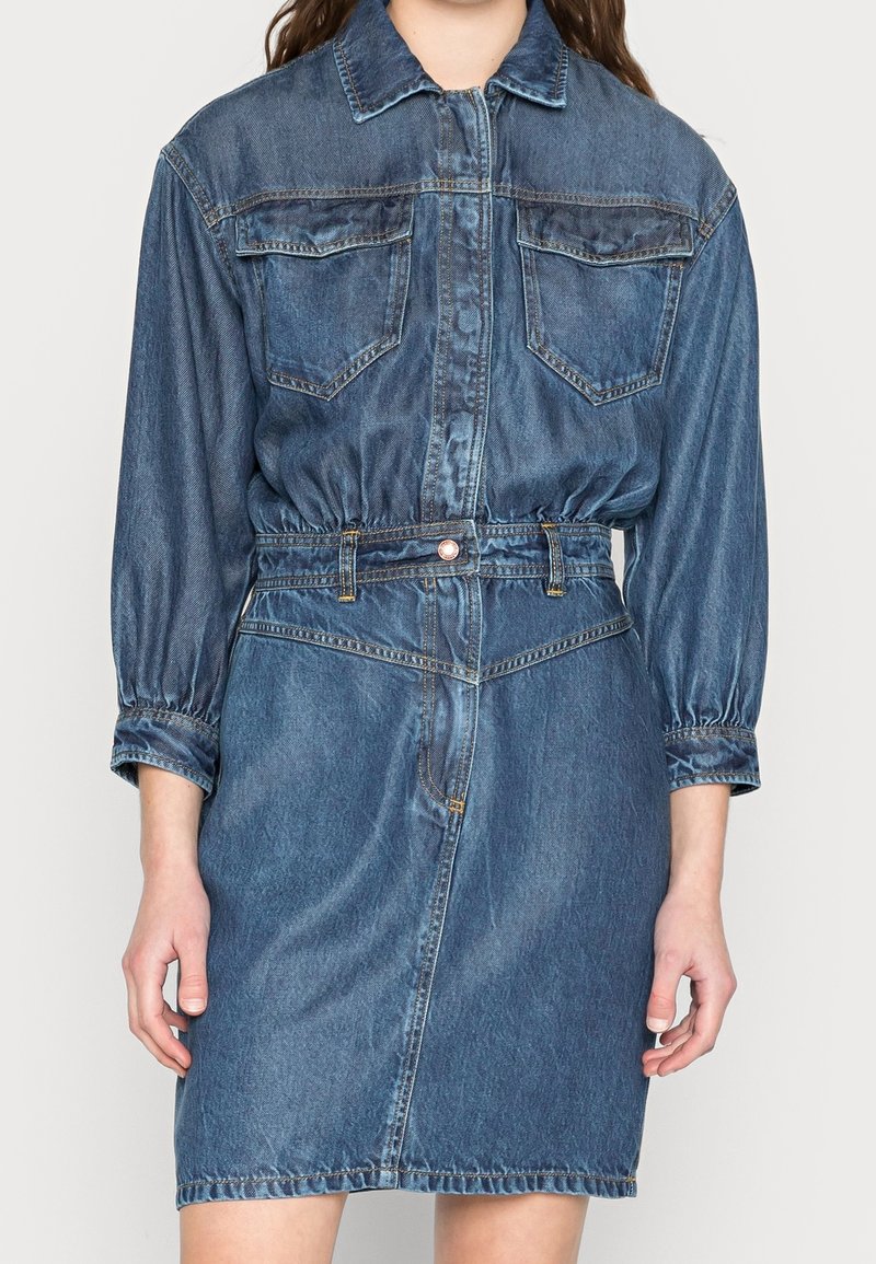 Denimmekko, jossa on pitkät puff-hihat, nappikaulus, kaksi rinta-taskua ja vyötärön kiristyminen vyöllä keskipesussa.