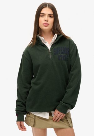 Dark green pullover with a high zip collar, featuring "SUPERDRY STATE" embroidered in dark blue on the chest. Cotton material and relaxed fit.
