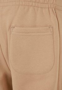 Nahaufnahme einer beigefarbenen Stoffhose mit sichtbaren Nähten an der Tasche und einem elastischen Bund darüber.