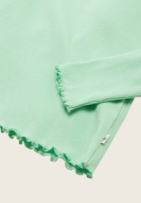 Mint zelena rebrasta pletena bluza z nabranim robom in robom rokavov, ki ima majhno oznako blagovne znamke na strani. Mehka tekstura, prilegajoča se zasnova.