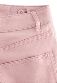 Vaaleanpunainen denimikangas napilla, ommelluilla yksityiskohdilla ja kahdella etutaskulla. Materiaalilla on teksturoitu, hienostunut ilme.
