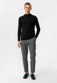 Zwarte lange mouwen coltrui gecombineerd met lichtgrijze slim-fit broek en zwarte instappers. Gladde textuur overal.