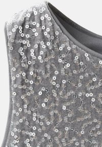 Harmaa hihaton toppi, jossa on paljeteilla koristeltu kuvio, jossa on ripoteltuja pyöreitä paljetteja, jotka luovat kimaltelevan efektin teksturoidun kankaan päällä.