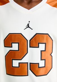 White basketball jersey with large orange number 23 and black Jumpman logo centered above the number.