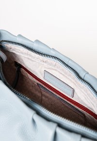 Helle blaue Lederhandtasche mit strukturiertem Finish, ausgestattet mit einer roten Reißverschlusstasche und beiger Innenauskleidung mit dezenten geometrischen Mustern.