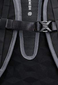 Mochila de tela negra con acentos de malla gris, un patrón texturizado, correas ajustables y un broche de plástico negro para el cierre.