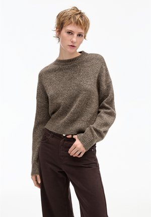 Pull en tricot marron avec un col rond et des poignets côtelés, associé à un pantalon taille haute marron foncé, sur fond blanc.