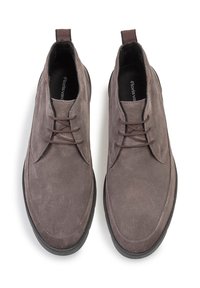 Zapatos de ante gris con una textura suave, puntera redonda y un diseño minimalista. Presentan cordones marrones y una suela de goma oscura.