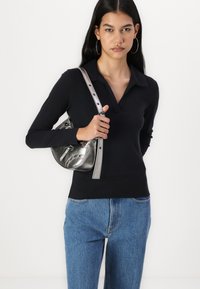 Crna majica dugih rukava s kragnom, uparena s svijetloplavim trapkama visokog struka i srebrenom metalnom torbicom preko tijela.