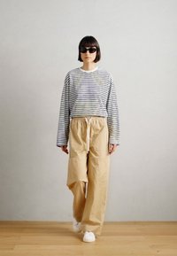 Ριγέ μακρυμάνικο μπλουζάκι με μαύρες και λευκές οριζόντιες ρίγες, συνδυασμένο με ανοιχτό μπεζ παντελόνι σε φαρδιά γραμμή και λευκά αθλητικά παπούτσια.