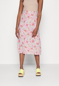 Saia midi floral com um fundo claro decorado com pequenas flores em rosa, vermelho e amarelo. Combinada com sapatos de salto bloco amarelos.