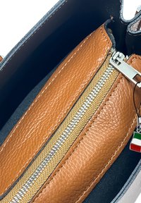 Bruine leren interieur met een ritsvak, gouden rits tanden, zwarte randen en een klein Italiaans vlagcharme. Gladde textuur, gestructureerd ontwerp.