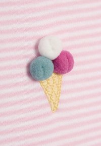 Cornet de glace brodé avec trois pompons colorés (rose, bleu et blanc) sur un fond rayé rose clair et blanc.