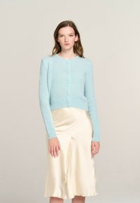 Light blue, cropped cardigan with long sleeves, round neck, and front buttons, paired with a cream satin slip skirt. Soft texture.
