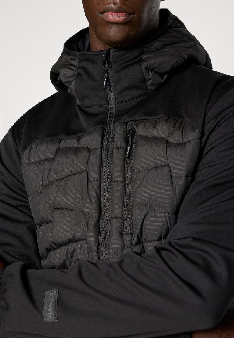 Czarna kurtka z wyściełanym panelem z przodu, kieszeniami na zamek błyskawiczny i kapturem. Wykonana z gładkiego materiału o lekko teksturowanej powierzchni.
