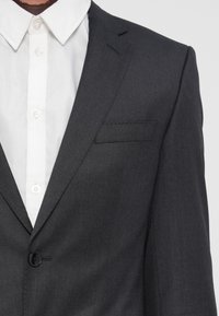 Schiefergraue Anzugjacke mit Reverskragen, einem Knopfverschluss und einer dezenten Textur; getragen über einem weißen Hemd mit Knöpfen.