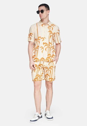 Korte mouwen beige shirt en bijpassende short met een oranje palmboomprint. Draag het met zwarte zonnebril en witte sneakers met blauwe accenten.