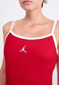 Raudonas raibais tank topas su baltu apvadu, išryškintas baltas Jordan logotipas ant krūtinės. Medžiaga atrodo lygi, su prigludusiu dizainu.
