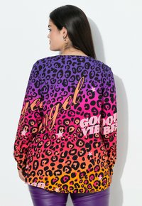 Multicolored long-sleeve shirt featuring a leopard print pattern in purple, pink, and orange, with text "Good Vibes" in white. Smooth texture.