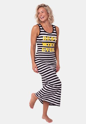Smiling woman with short blonde hair wearing a black and white striped sleeveless dress with yellow text "BEST WIFE EVER" barefoot.