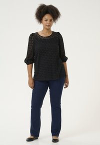 Zwart gemêleerd top met een ronde hals en driekwart pofmouwen, gecombineerd met donkerblauwe rechte jeans en zwarte flats.