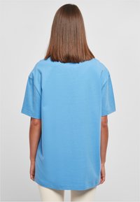 Světle modré oversized tričko s krátkými rukávy, vyrobené z měkké a hladké tkaniny. Má kulatý výstřih a rovný lem.