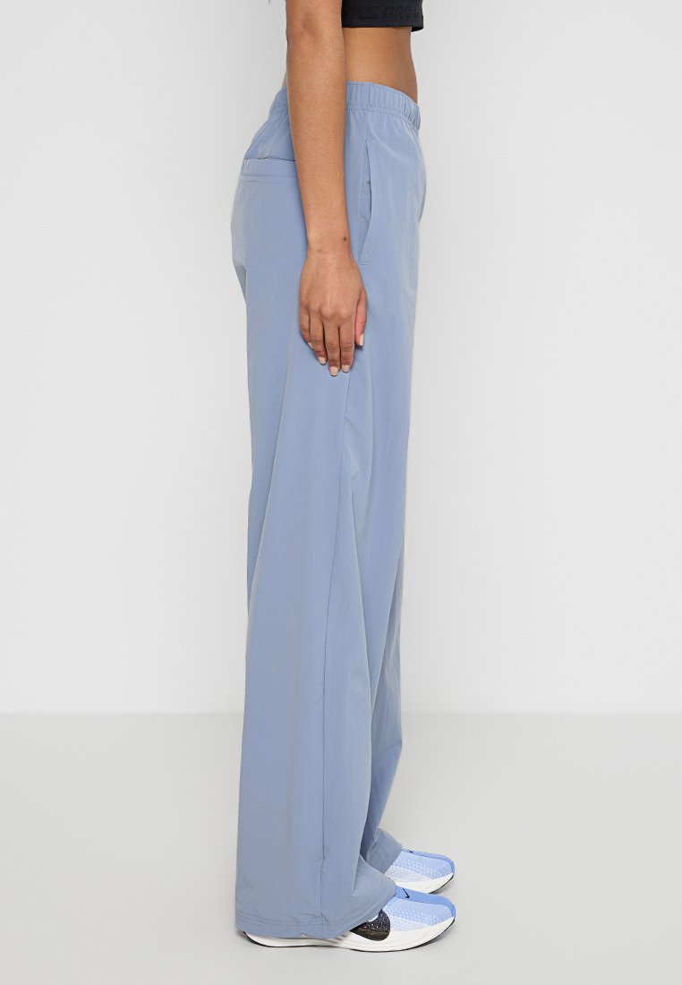 Pantalones sueltos de color azul claro con cintura elástica, bolsillos laterales y textura suave, combinados con zapatillas deportivas blancas y azules.