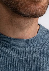Lichtblauwe gestructureerde trui met een geribde ronde halslijn, met een close-up van de stof en halsdetail, tegen een neutrale achtergrond.