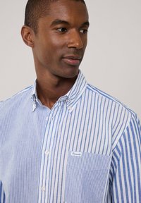 Blau-weißer gestreifter Button-Up-Hemd mit einer Tasche. Der Stoff sieht leicht und mit einer glatten Textur aus. Markenlogo auf der Tasche.