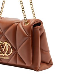 Bolso de mano marrón acolchado de piel sintética con cadena dorada y detalle de logo. Presenta una textura suave y un diseño angular. Combina elegancia y funcionalidad.