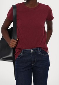 Camiseta burdeos de manga corta hecha de tela suave, combinada con pantalones vaqueros azul oscuro que presentan costuras clásicas y un bolsillo lateral.