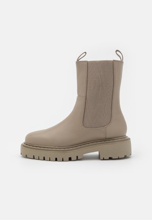 Bottine beige en cuir lisse avec des panneaux latéraux élastiques, une languette de tirage bouclée et une semelle en caoutchouc robuste avec crampons.