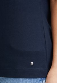 Granatowa bawełniana koszulka z gładką teksturą, z metalicznym logo w srebrnym kolorze przy dole oraz prostym, klasycznym wzorem.