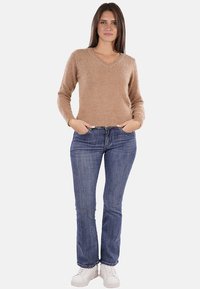 Maglione beige a maglia con scollo a V, maniche lunghe e una consistenza morbida, abbinato a jeans blu a gamba dritta e sneakers bianche.