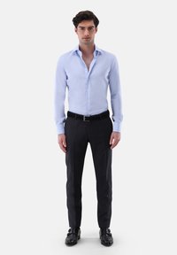 Hellblaues Langarmhemd mit spitzem Kragen und Knöpfen an der Vorderseite, kombiniert mit maßgeschneiderten schwarzen Hosen und schwarzen Schuhen.